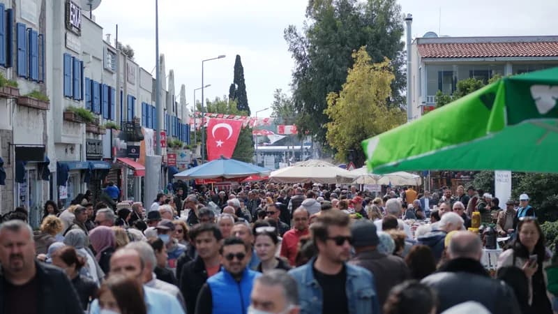 İki yanı dükkân ve tezgâh olan sokakta yoğun kalabalık; ortada asılı bir Türk bayrağı