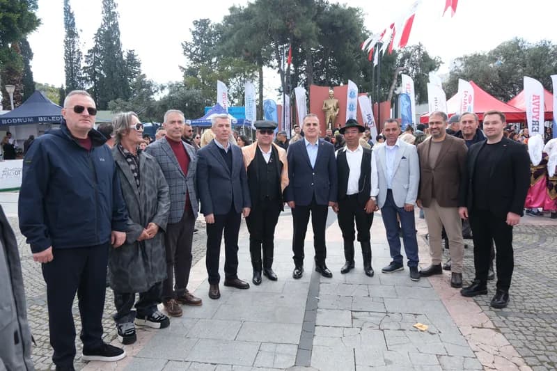 Festival açılışında sıra hâlinde duran davetliler; arkada bayraklar, kurum çadırları ve bir heykel