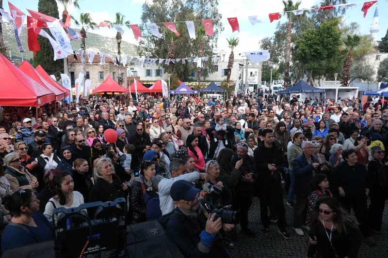 Sahneye dönmüş yüzlerce kişilik kalabalık; üstte Türk bayrakları ve festival flamaları, arkada çadırlar ve palmiyeler