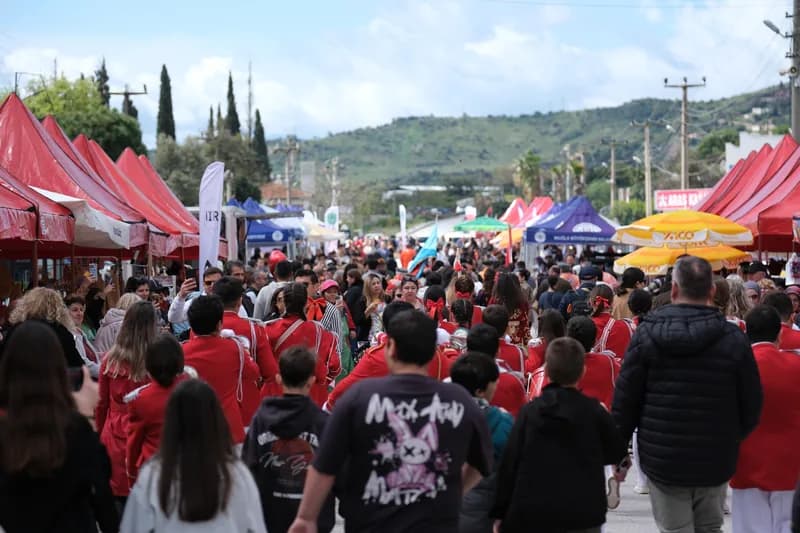 Kırmızı çadırların dizildiği sokakta ilerleyen kalabalık; kırmızı kostümlü bir folklor ekibi ve arkada Bodrum tepeleri